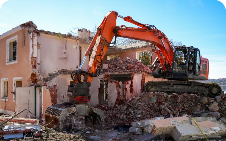 Excavator demolishing a partially collapsed house.