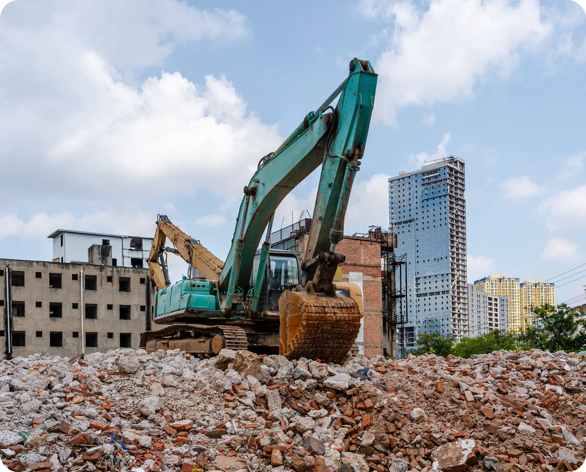 Excavator on rubble with city buildings background.