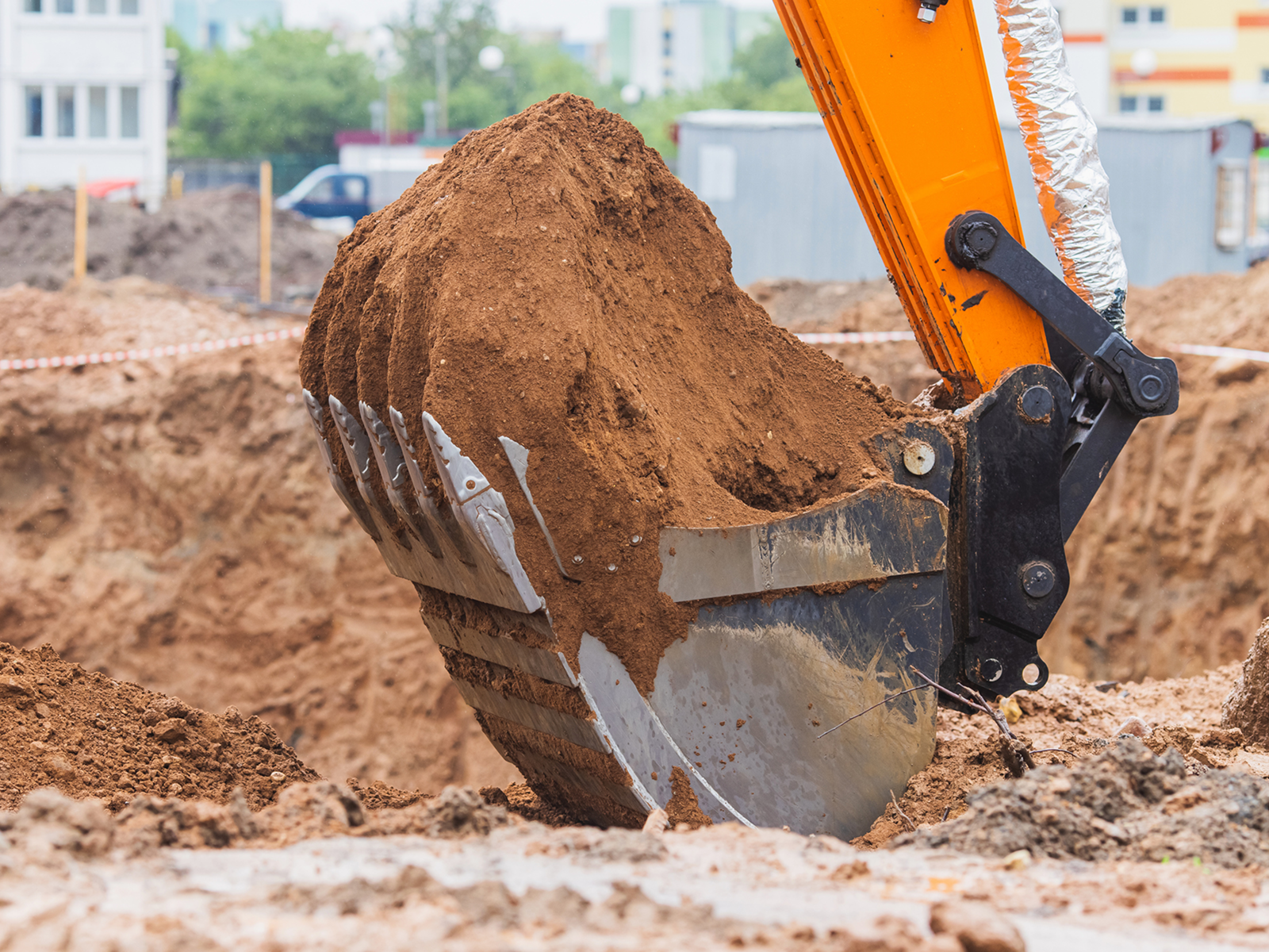 Excavator bucket lifting soil at construction site.