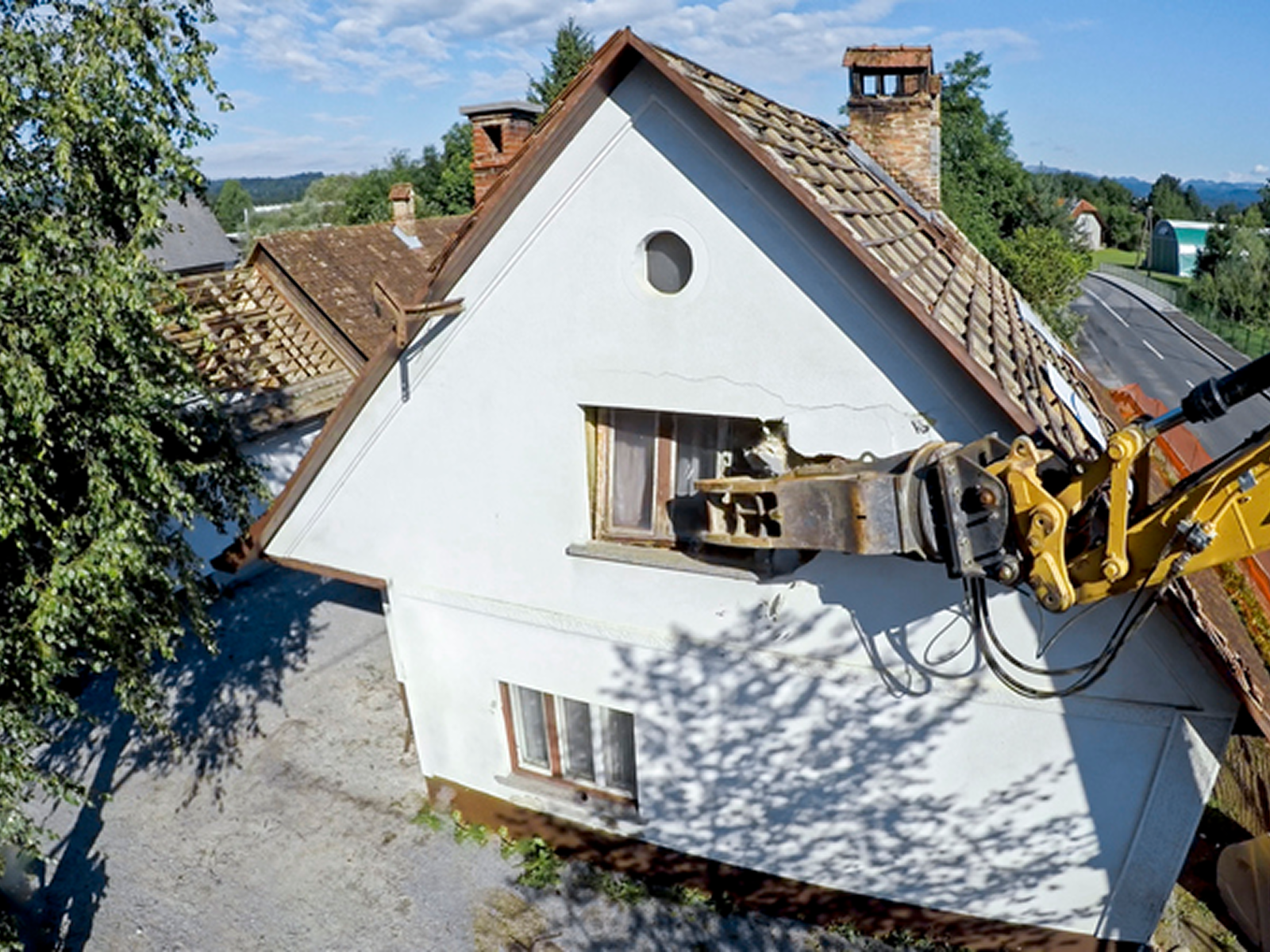 Excavator demolishing white house roof.