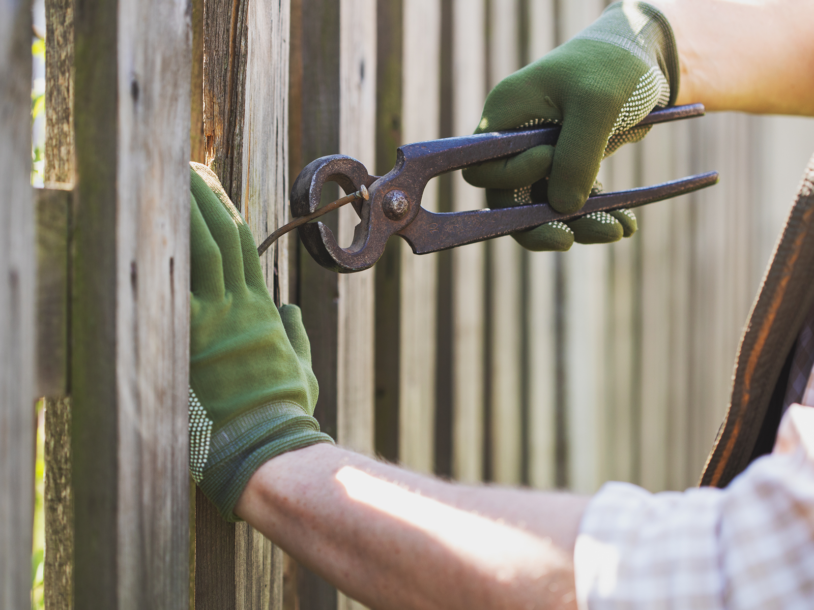 Person fixing wooden fence with pliers.